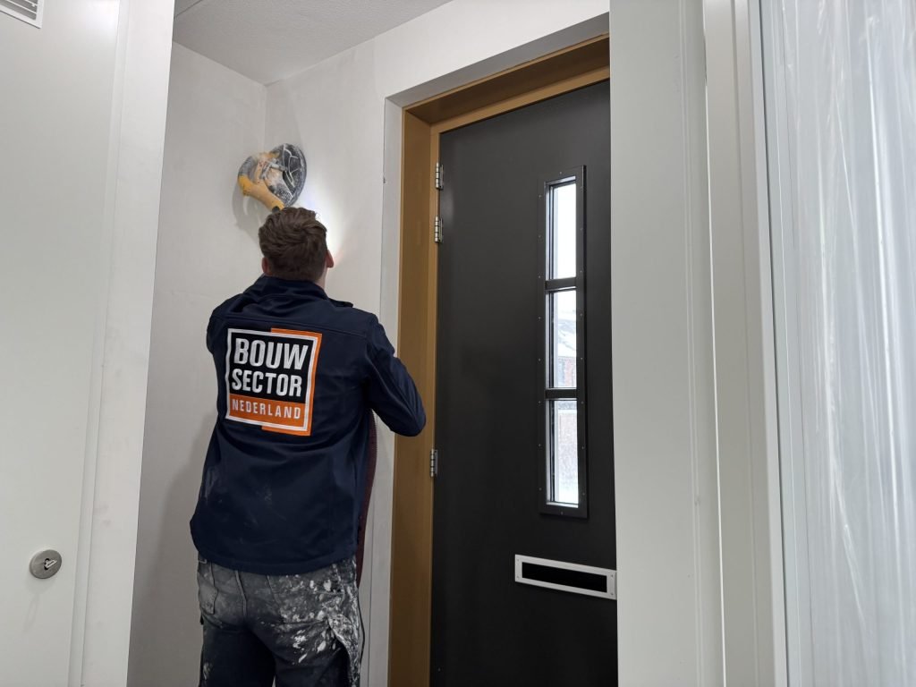 Vakman van Bouwsector Nederland met een wandschuurmachine aan de wand boven een voordeur