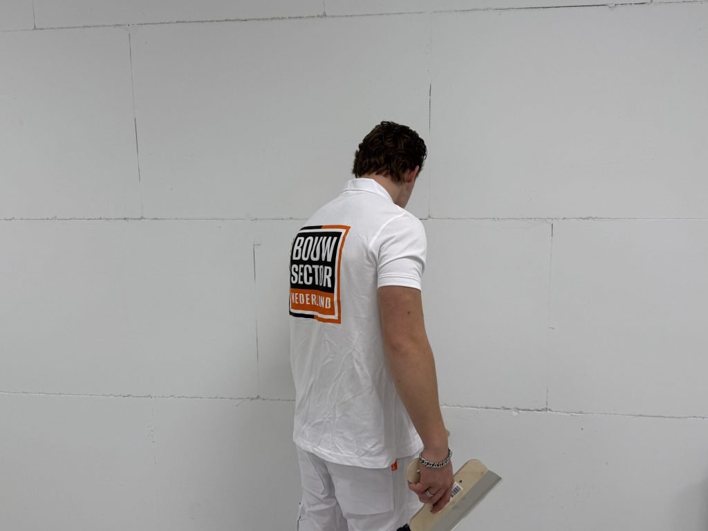 Stukadoor van Bouwsector Nederland met een plakspaan bij een kale blokkenwand waarop de voegen nog zichtbaar zijn