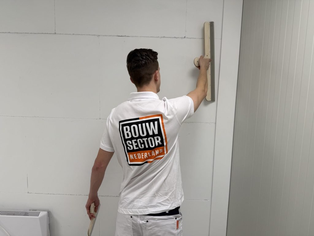 Stukadoor in wit werkpak strijkt met een brede spaan over een wand van gipsblokken