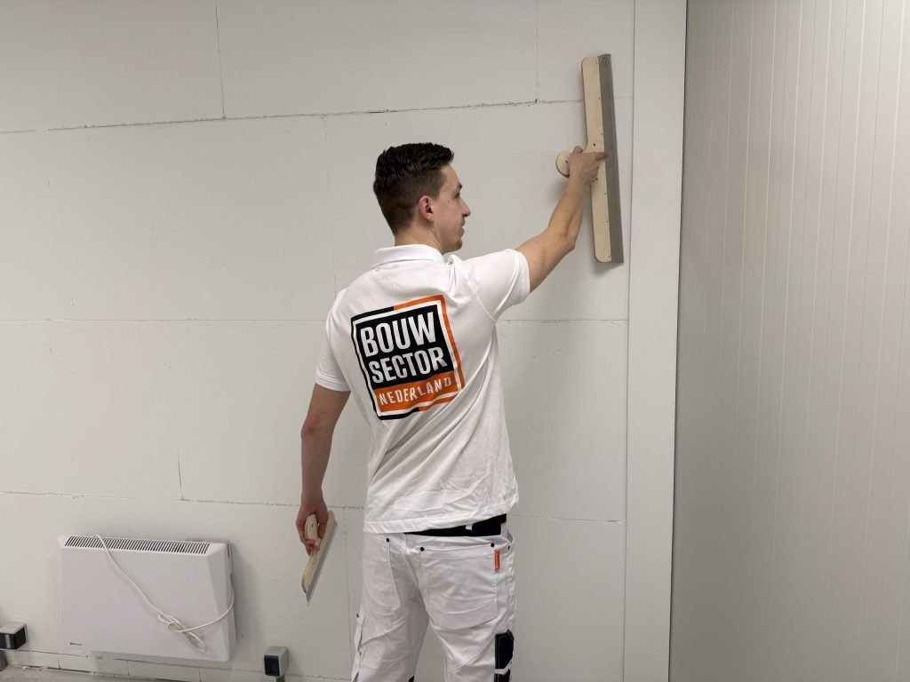 Stukadoor werkt de bovenkant van een wand af met een lange spaan, vlak onder het plafond