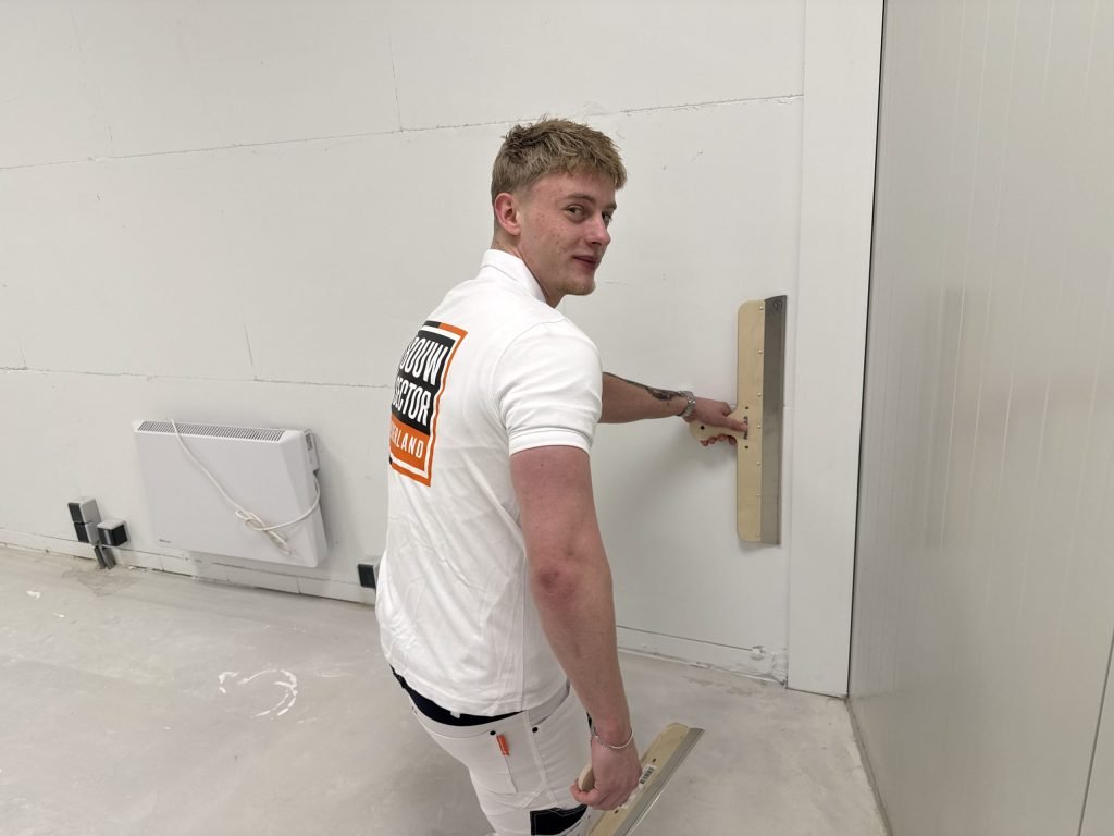 Stukadoor kijkt om terwijl hij met een spaan de natte pleister op een lange wand gladstrijkt