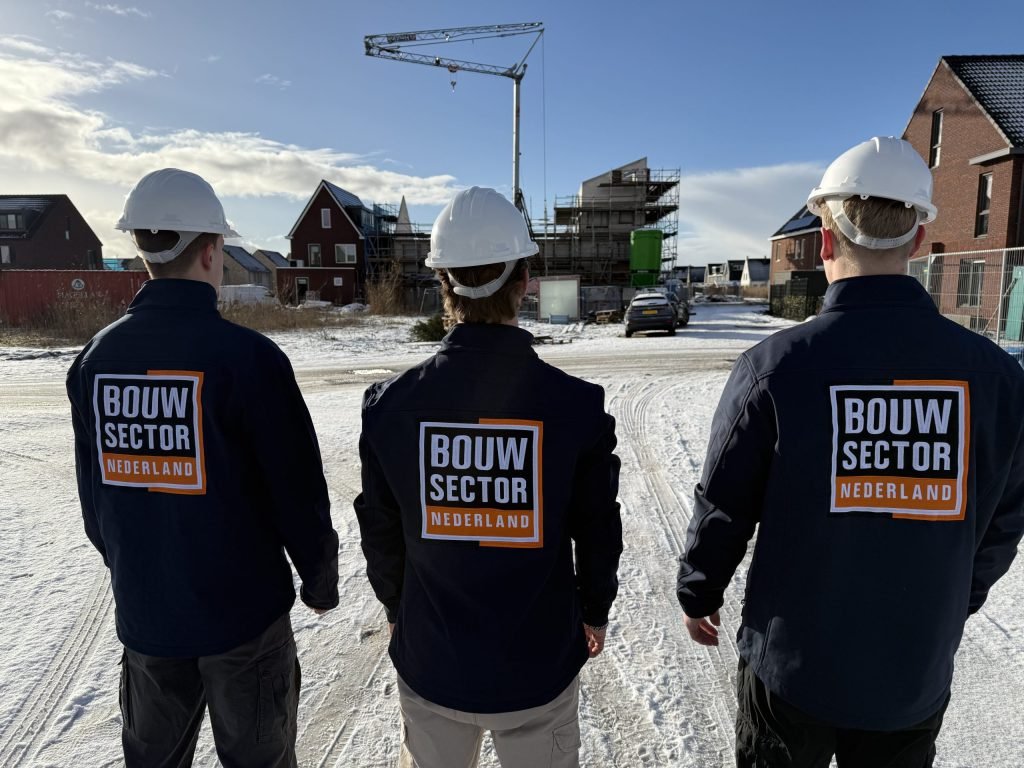 Drie vakmensen van Bouwsector Nederland met witte helm kijken naar rijen woningen in aanbouw op een winterdag